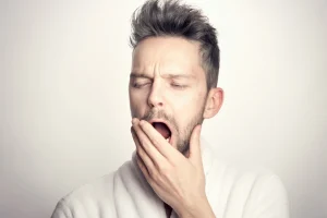 Tired man yawning and covering his mouth, illustrating bad breath concerns and the importance of dental care